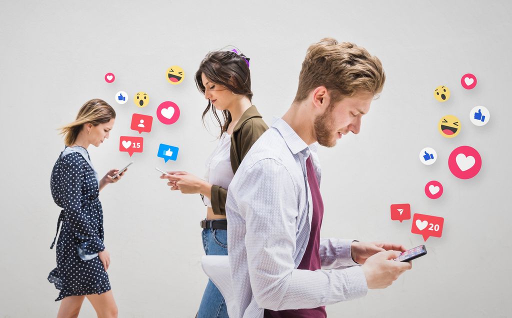 Pessoas andam na olhando o celular, com ícones de reações