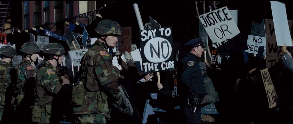 Cartazes de "Diga não à cura" durante manifestações contra a cura mutante, em cena de X-Men 3: O Confronto Final (2006)