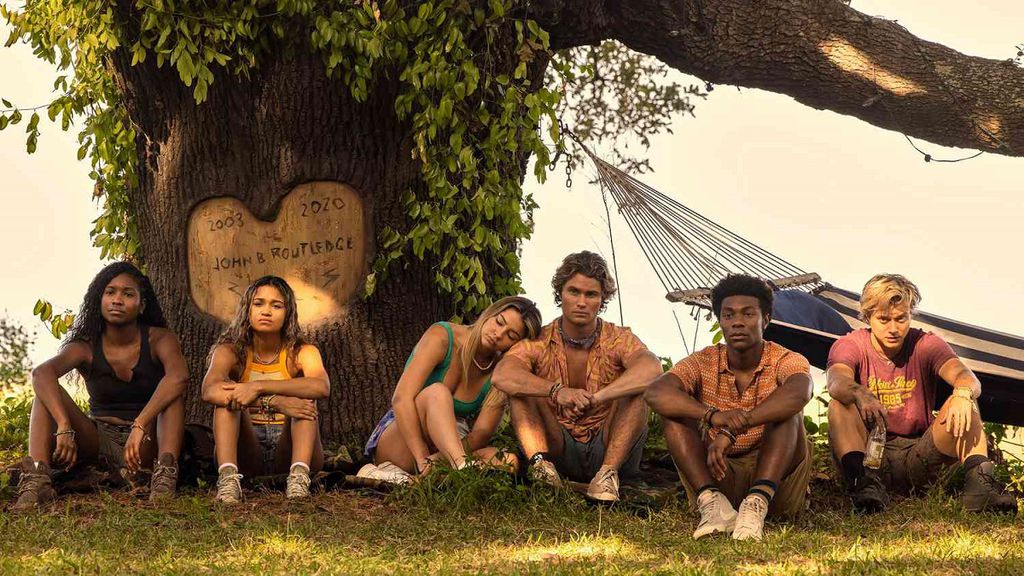 Uma foto com os protagonistas da série Outer Banks sentado embaixo de uma árvore.