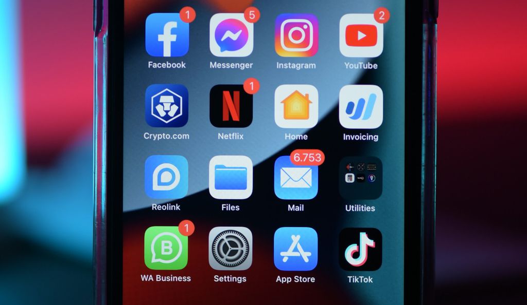 Mão segurando um celular com notificações na tela, em um ambiente de escritório e focada no aparelho