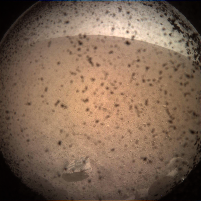 Primeira imagem enviada pela InSight, ainda sem remover o protetor de suas lentes e momstrando muita poeira resultante de seu pouso (Foto: NASA)