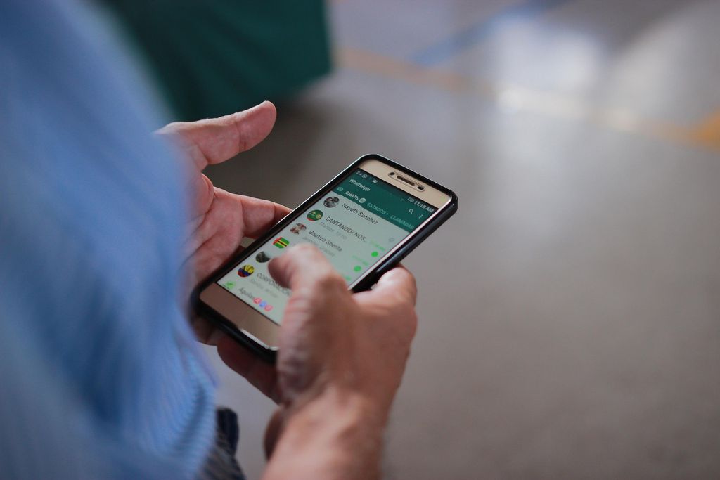 Homem segura um celular com o WhatsApp aberto cheio de mensagens