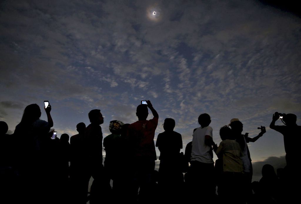 Não vá fazer como o pessoal aí da foto, observando o eclipse sem proteção ocular ou pelo smartphone! (Foto: Beawiharta Beawiharta / Reuters)