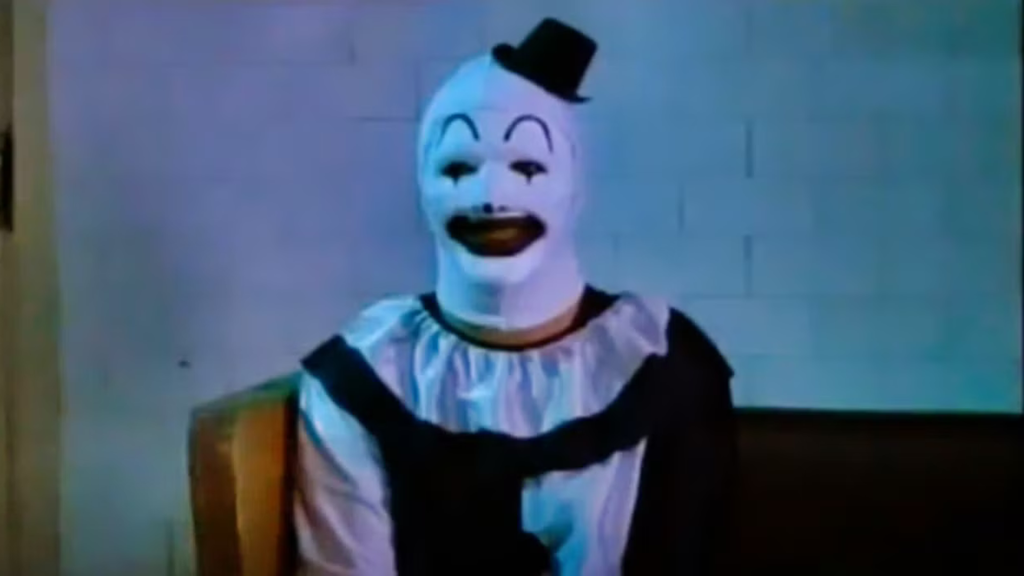 O palhaço Art, da franquia Terrifier, aparece sorrindo para a câmera. 