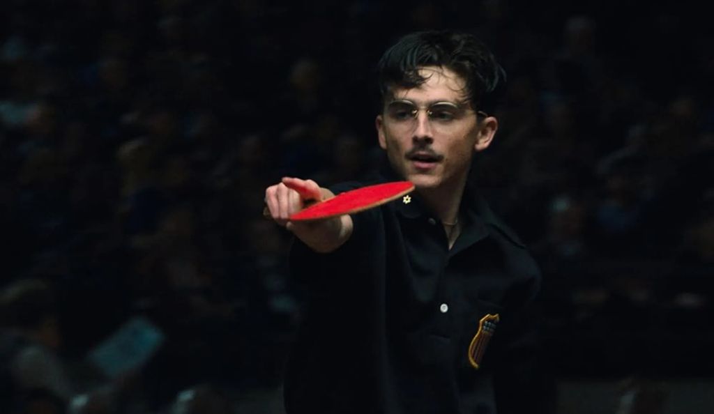Cena do filme Marty Supreme com Timothée Chalamet com uma raquete de pinh-pong na mão