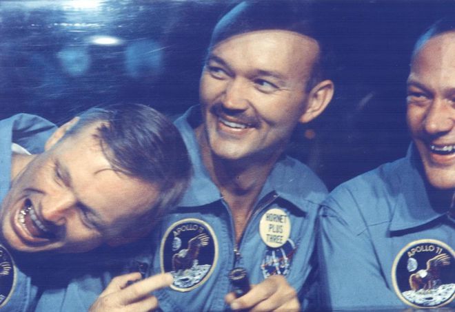 Os três astronautas já de volta à Terra, em foto tirada através da janela da câmara de contenção onde ficaram durante 21 dias (Imagem: NASA)