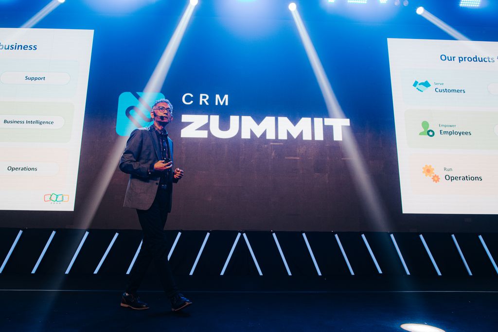 Palco do CRM Zummit com a logo no fundo e o CSO da Zoho em abertura do evento