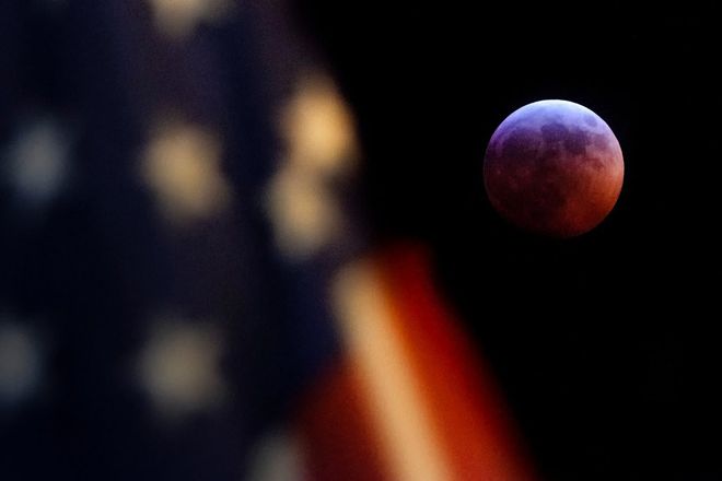 A bandeira dos Estados Unidos desfocada à frente da Lua durante o eclipse (Foto: David Ake/Associated Press)