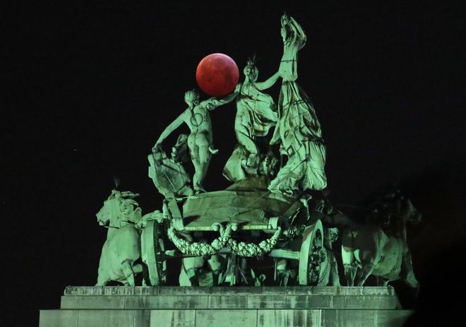 A lua avermelhada acima de uma escultura na Bélgica (Foto: Yves Herman/Reuters)