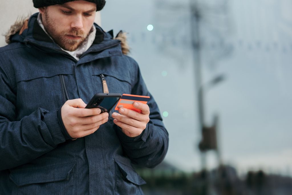 Pessoa segurando um cartão de crédito enquanto mexe no celular