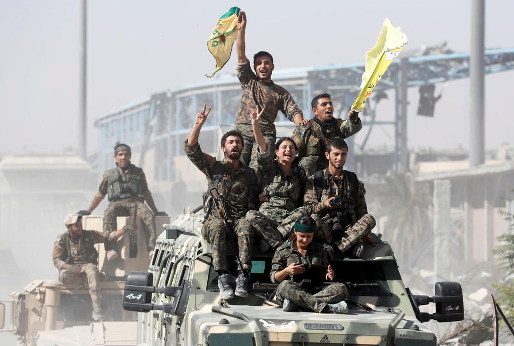 Membros da resistência curda celebram vitória em cima de veículo militar fornecido pelos Estados Unidos (Imagem: Erik de Castro/Reuters)