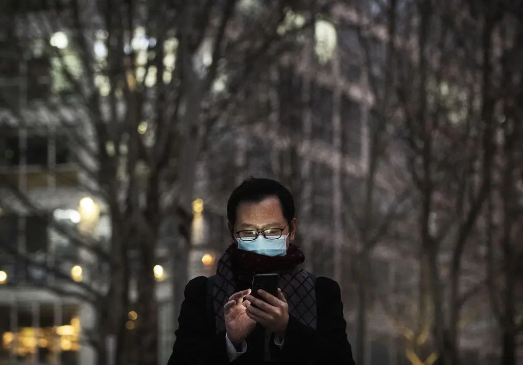 Homem chinês olhando mexendo no celular com uma máscara cobrindo a boca (Foto: Reprodução/Buzzfeed News)