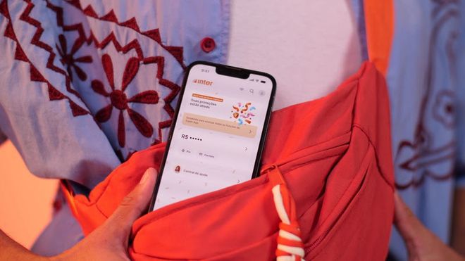 Uma bolsa com um celular guardado nela; na tela, é possível ver o Modo Carnaval do aplicativo do Banco Inter