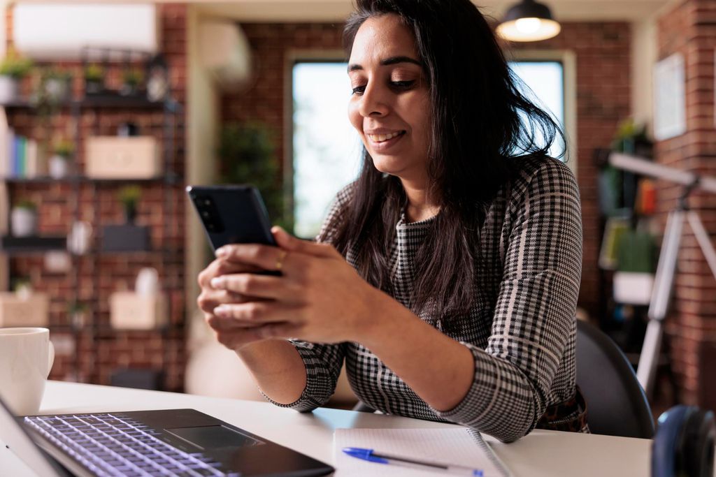  Freelancer feminino trabalhando no aplicativo de smartphone e usando laptop