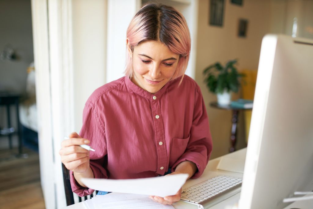 Empreendedora olha um papel e está sentada em frente a uma tela de computador