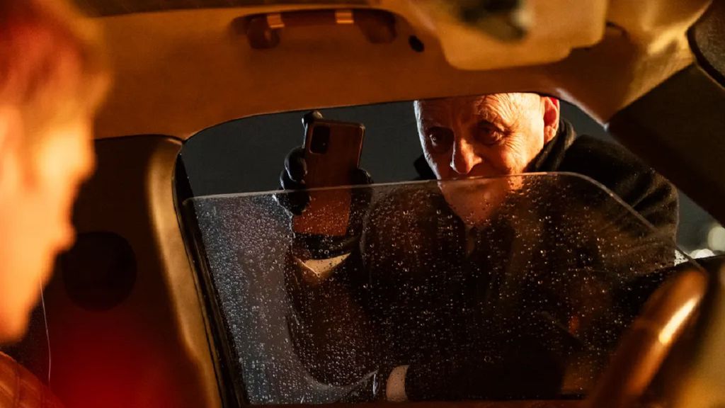 Homem parado na janela de um carro segurando um celular no meio da noite